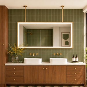 May include: A double vanity bathroom featuring a wooden cabinet with six drawers and two doors, topped with two white rectangular sinks. Above, a rectangular LED-lit mirror hangs from two gold ceiling mounts against olive green tiled walls.