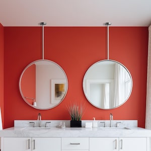 Pode incluir: Uma casa de banho moderna com uma parede vermelha vibrante. Dois espelhos redondos com moldura prateada pendem sobre uma vaidade branca com bancada de mármore. A vaidade tem puxadores prateados e uma floreira retangular preta.