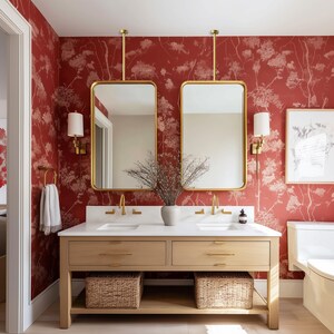May include: A bathroom with a red floral wallpaper backdrop. Two rectangular gold-framed mirrors hang above a light wood vanity with a white countertop. Wicker baskets are below the vanity. Gold fixtures and sconces complete the design.