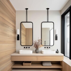 May include: A modern bathroom vanity with two rectangular mirrors suspended from the ceiling. The mirrors have black frames and are positioned above white rectangular sinks. The vanity is made of light wood, with a lower shelf and a basket.