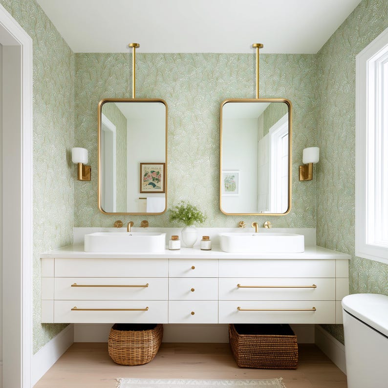 May include: A modern bathroom with a white vanity, two rectangular mirrors with gold frames, and a light green patterned wallpaper. The vanity has two sinks, gold fixtures, and woven baskets below. The room is well-lit with sconces and natural light.