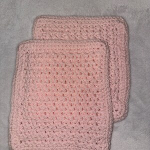 May include: Two pink crocheted squares, likely for a baby blanket or other craft project.