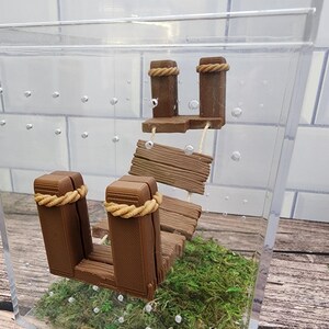 May include: A miniature wooden dock with a rope detail, set in a clear acrylic box with green moss and small white bubbles.