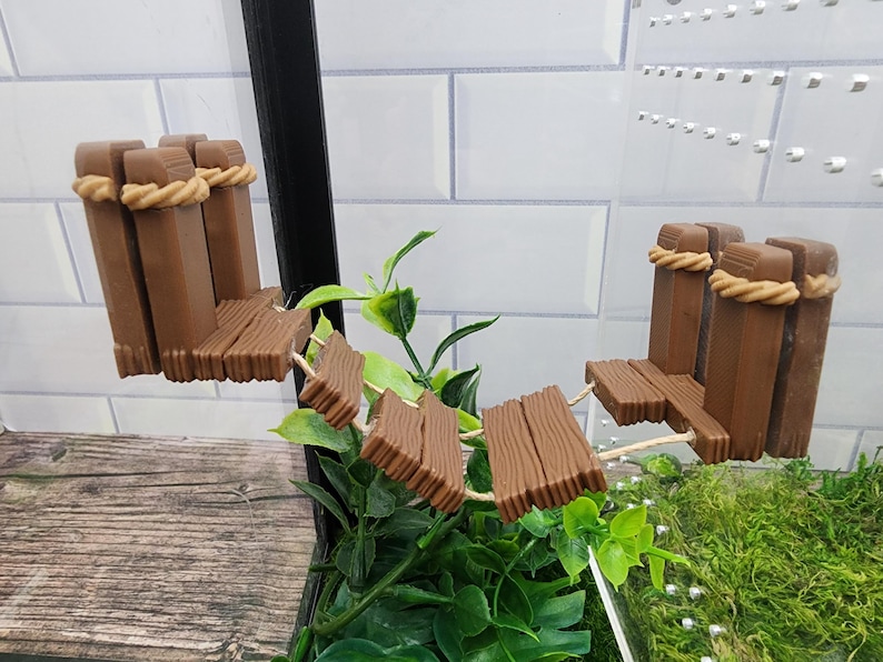 May include: A brown wooden bridge with rope railings for a reptile terrarium. The bridge is made of multiple pieces of wood and is curved to fit the terrarium.