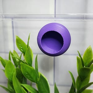 May include: Purple plastic hide for small animals, such as reptiles or amphibians. The hide has a round shape with a hole in the centre.