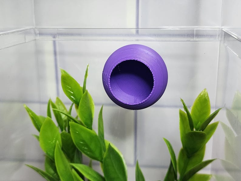 Puede incluir: Escondite de pl&aacute;stico morado para animales peque&ntilde;os, como reptiles o anfibios. El escondite tiene una forma redonda con un agujero en el centro.