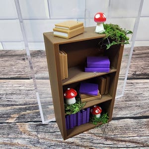 May include: A miniature brown bookshelf with three shelves, filled with tiny books, purple stacks, and red and white mushroom figurines. Green moss adds a natural touch to the whimsical scene. A charming decorative piece.