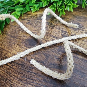 Può includere: Primo piano di una corda in fibra naturale di colore beige chiaro, su una superficie di legno.