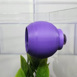 Puede incluir: Una bomba de aire de pl&aacute;stico morado para un acuario, unida al lado del tanque.