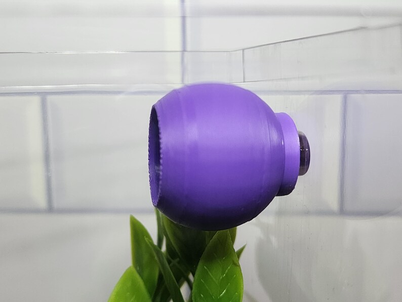 Puede incluir: Una bomba de aire de pl&aacute;stico morado para un acuario, unida al lado del tanque.