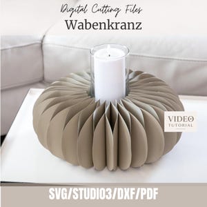 以下が含まれることがあります： Wabenkranz用のデジタルカットファイル。ベージュのハニカムペーパーリースの中央にガラスシリンダーがあり、白いピラーキャンドルが入っています。テキストにはDigital Cutting Files、Wabenkranz、Video Tutorial、SVG/STUDIO3/DXF/PDFと記載されています。