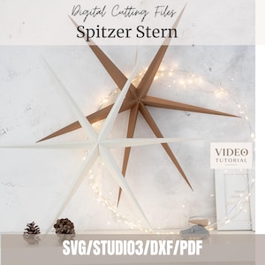 Op de afbeelding: Twee grote, meerpuntige papieren sterren in wit en bruin, met de tekst Digital Cutting Files Spitzer Stern, SVG/STUDIO3/DXF/PDF en Video Tutorial. De sterren worden verlicht door dunne, gloeiende lichtsnoeren met kleine lampjes.