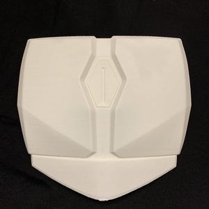 Op de afbeelding: Een wit, stijf, geometrisch borstplaatonderdeel met een symmetrisch ontwerp met schuine panelen en een centrale verticale rechthoekige inkeping. Het stuk heeft een brede, platte bovenrand die taps toeloopt naar een punt.