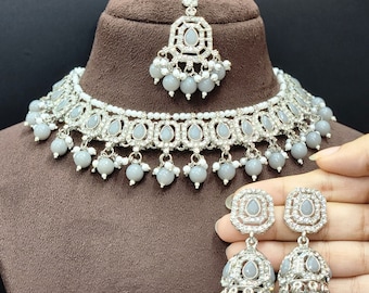 May include: A silver-toned jewelry set featuring a necklace, earrings, and a headpiece. The necklace and earrings have gray teardrop-shaped stones and white bead accents. The set is displayed on a brown mannequin head.