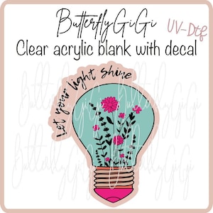 May include: Clear acrylic blank with decal featuring a lightbulb design. The lightbulb is filled with pink flowers and greenery, with the words "Let your light shine" in a script font. The text "Butterfly GiGi" is at the top.