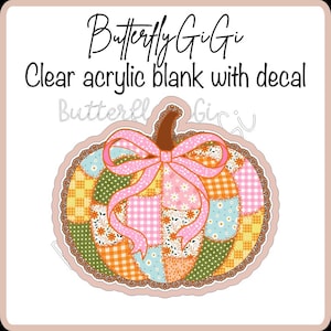 May include: A clear acrylic blank featuring a pumpkin-shaped decal with a patchwork design in shades of orange, pink, blue, and green. The pumpkin is adorned with a large pink bow and brown stem. Text reads ButterflyGiGi Clear acrylic blank with decal.