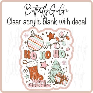 May include: Clear acrylic blank with a Christmas-themed decal. The design includes a Christmas stocking, ornaments, stars, a Christmas tree, and the words "HO HO HO" and "Merry Christmas". The design is in shades of pink, red, and green.