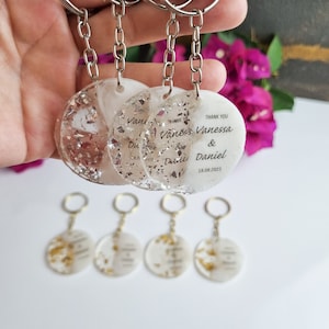 May include: Set of six white round keychains with gold and silver glitter embedded in the resin. The keychains have the text "Thank You Vanessa & Daniel 18.08.2023" printed on them.