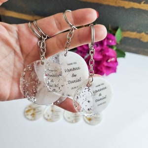 May include: Three clear round keychains with silver glitter embedded in the resin. Each keychain has a silver metal ring and chain. The keychains are personalized with the text "Thank You Vanessa & Daniel" and the date "18.08.2023".