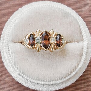 May include: A gold ring featuring three marquise-cut brown gemstones arranged horizontally, accented by four small round clear stones set between the larger gems. The metal band has a decorative, pointed prong setting holding each stone securely in place.