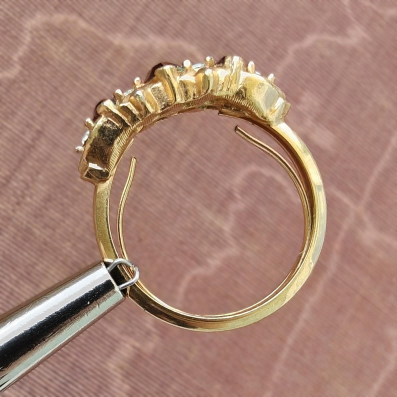 May include: A gold ring featuring a curved row of multiple small, clear, faceted stones set along the top band. The metal band is polished and circular, showing a side profile view of the setting where the stones are secured in individual prongs.