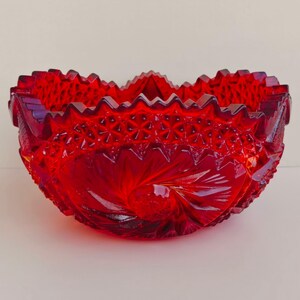 May include: A vibrant red glass bowl with a detailed, textured surface. The bowl features a scalloped rim and intricate patterns, including starburst and leaf designs. The bowl is a deep, rich red color.
