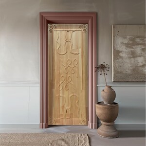 May include: A light-colored wooden door with carved snake and knot designs, set within a pink-framed doorway. The door is the focal point, with a neutral-toned wall and a decorative vase on a pedestal nearby. A rug is visible on the floor.