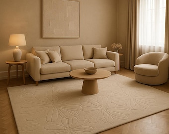 May include: A beige living room with a beige sofa, a coffee table, a side table, a lamp, a rug, and a chair. The rug has a floral pattern.