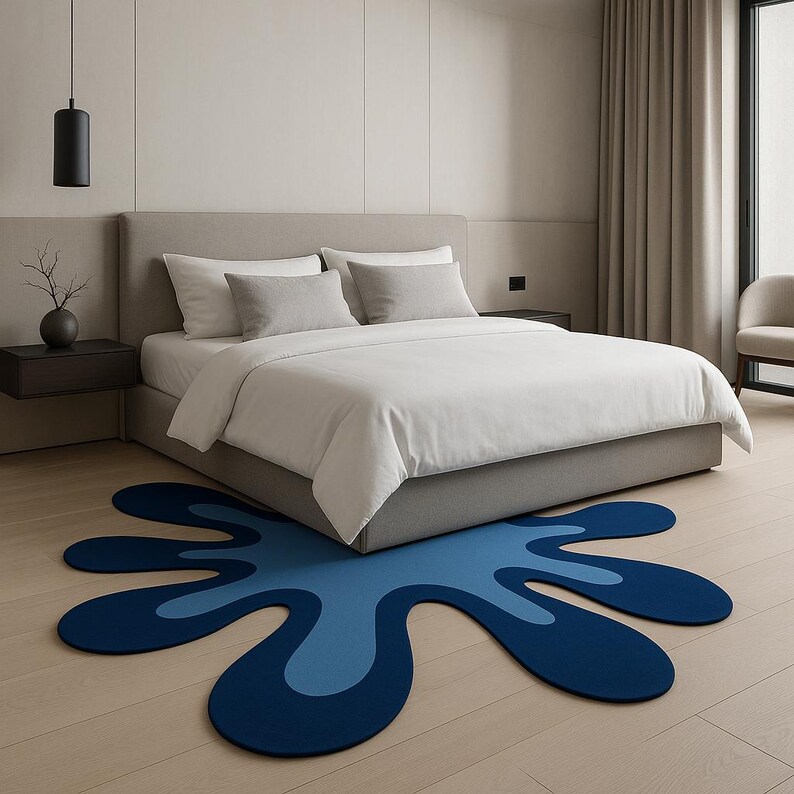 Op de afbeelding: Een moderne slaapkamer met een groot bed, wit beddengoed en grijze kussens. Een uniek, abstract tapijt in blauwtinten ligt op de lichte houten vloer voor het bed en voegt een vleugje kleur en een eigentijdse uitstraling toe aan de kamer.