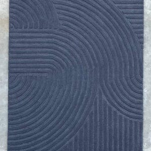 May include: A dark blue rug with a geometric pattern of curved lines. The rug has a textured surface and a modern design.