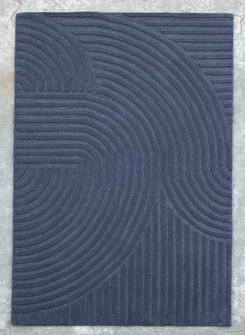 May include: A dark blue rug with a geometric pattern of curved lines. The rug has a textured surface and a modern design.