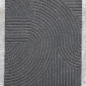 May include: A black and grey area rug with a geometric pattern of curved lines.