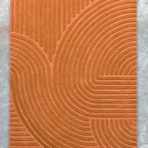 May include: A burnt orange rug with a geometric pattern of curved lines. The lines are raised and create a textured surface.