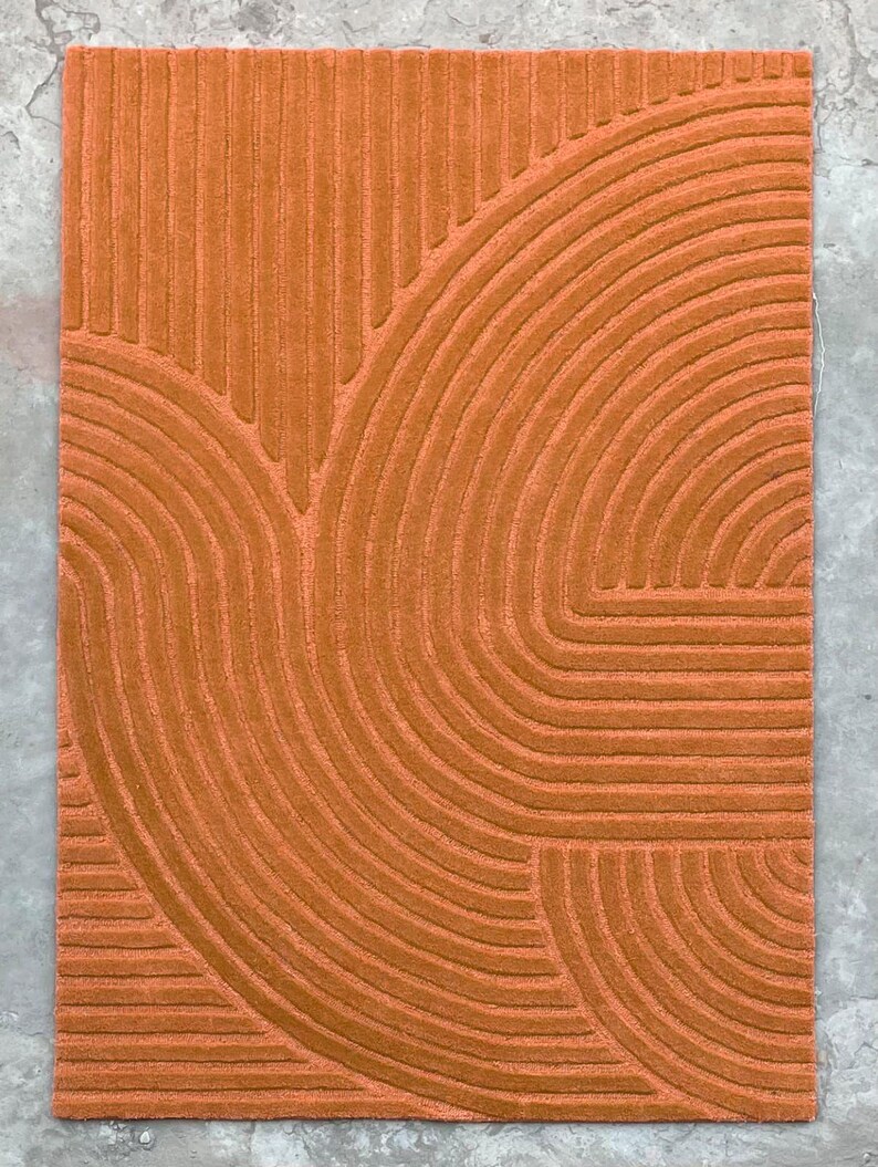 May include: A burnt orange rug with a geometric pattern of curved lines. The lines are raised and create a textured surface.