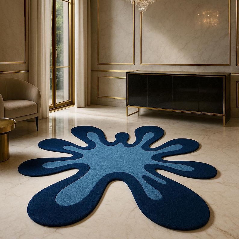 Op de afbeelding: Een abstract tapijt in een spatontwerp. Het tapijt heeft een donkerblauwe buitenrand, een middelblauwe binnenkant en een lichtere blauwe kern. Het tapijt ligt op een marmeren vloer in een kamer met een zwarte kast.