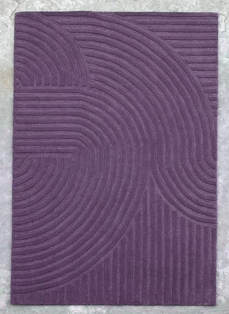 May include: A purple rug with a geometric pattern of curved lines. The rug has a textured surface and a modern design.