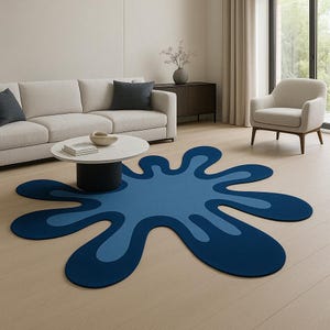 Op de afbeelding: Een blauw, abstract gevormd tapijt met een donkerblauwe omtrek en een lichtblauw interieur. Het tapijt ligt op een lichte houten vloer in een woonkamer. Het unieke ontwerp van het tapijt voegt een moderne touch toe aan de inrichting van de kamer.