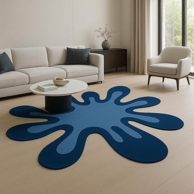 Op de afbeelding: Een blauw, abstract gevormd tapijt met een donkerblauwe omtrek en een lichtblauw interieur. Het tapijt ligt op een lichte houten vloer in een woonkamer. Het unieke ontwerp van het tapijt voegt een moderne touch toe aan de inrichting van de kamer.