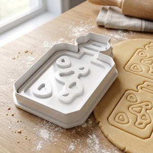 Könnte beinhalten: Ein weißer Kunststoff-Ausstecher in Form einer Parfümflasche mit ausgeschnittenen Details. Daneben ein Teigstück mit der eingedrückten Keksform. Der Ausstecher liegt auf einer mit Mehl bestäubten Holzoberfläche.