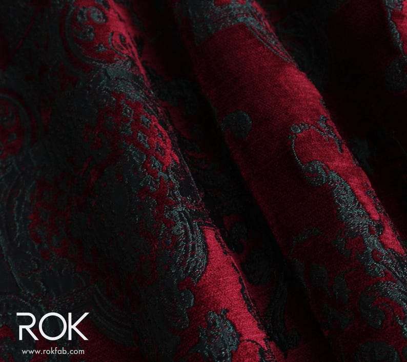 May include: Close-up of a deep red fabric with a black, ornate damask pattern. The fabric is folded, showing the texture and depth of the design. The word "ROK" is visible in white text at the bottom left.