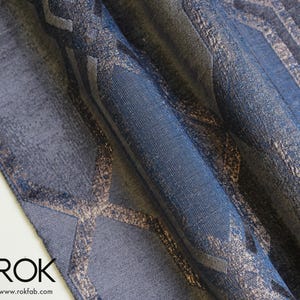 May include: Close-up of a rolled-up fabric with a geometric pattern. The fabric features a blend of blue and gray tones with metallic gold accents. The word "ROK" and the website address are visible at the bottom.