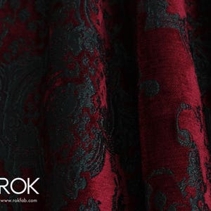 May include: Close-up of a luxurious fabric with a damask pattern. The fabric features a deep burgundy red and black color scheme. The pattern is a classic floral design, creating a rich and elegant texture. The fabric is likely used for upholstery or drapery.