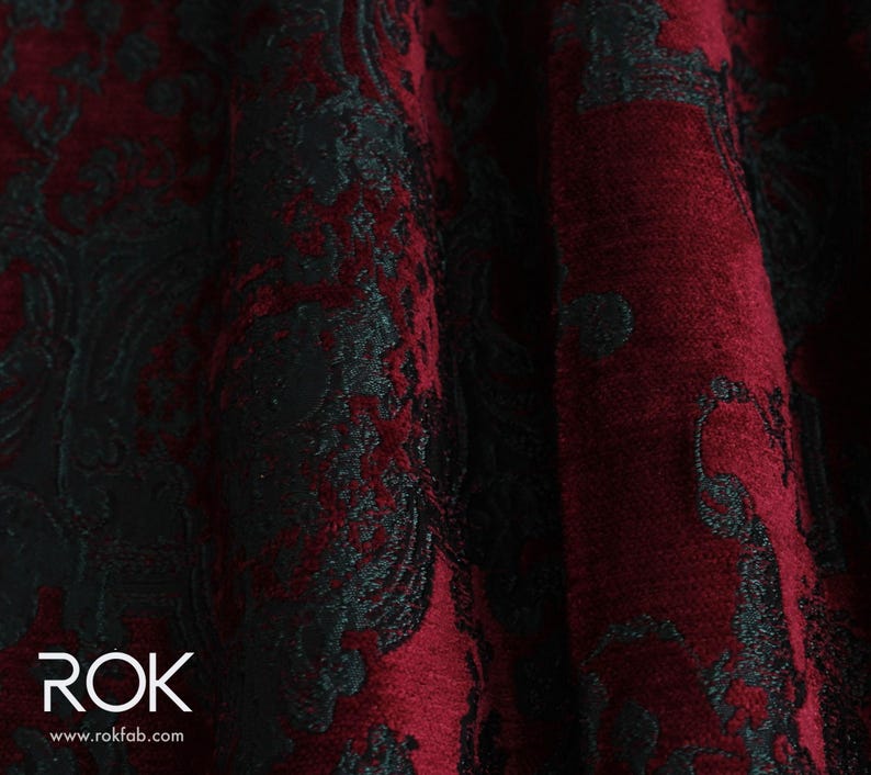 May include: Close-up of a luxurious fabric with a damask pattern. The fabric features a deep burgundy red and black color scheme. The pattern is a classic floral design, creating a rich and elegant texture. The fabric is likely used for upholstery or drapery.