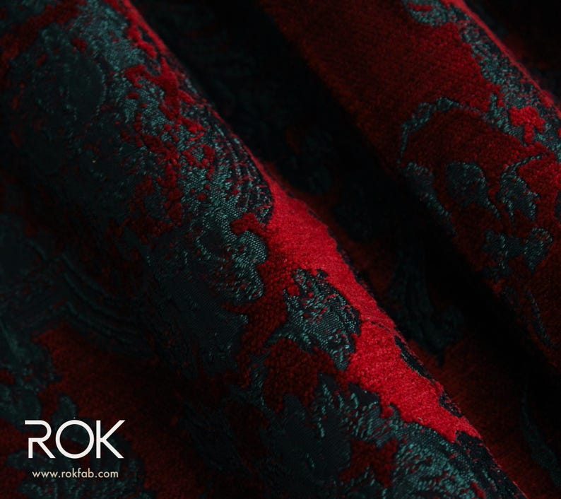 May include: Close-up of a textured fabric with a damask pattern. The fabric features a deep red background with a contrasting dark teal floral design. The word "ROK" and website address are visible in the lower left corner.