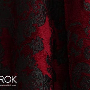 May include: Close-up of a fabric with a deep red background and a black floral pattern. The fabric has a textured appearance, with the black pattern overlaying the red. The logo "ROK" and website address are visible in the bottom left corner.
