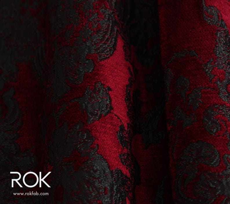 May include: Close-up of a fabric with a deep red background and a black floral pattern. The fabric has a textured appearance, with the black pattern overlaying the red. The logo "ROK" and website address are visible in the bottom left corner.