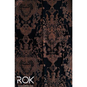 May include: Close-up of a dark fabric with an ornate, repeating pattern in shades of bronze and black. The design features swirling floral and scroll motifs. The text "ROK" and website address www.rokfab.com are visible at the bottom.