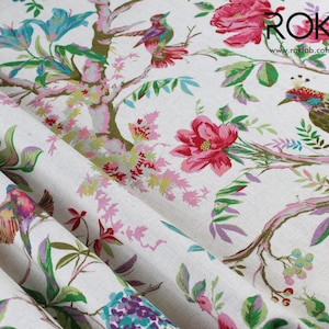 May include: Close-up of a white fabric with a floral and bird pattern. The design features pink, red, and blue flowers, along with colourful birds perched on branches. The fabric has a textured appearance, with the text "ROK" and website address visible.