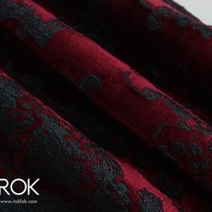 May include: Close-up of a burgundy fabric with a black floral pattern. The fabric is folded, showing the texture and design. The text "ROK" and website address are visible in the lower left corner.