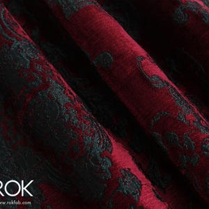May include: Close-up of a fabric with a damask pattern. The fabric is a deep burgundy color with a black, ornate design. The fabric is folded, showing the texture and depth of the material. The logo "ROK" and website address are visible in the bottom left corner.